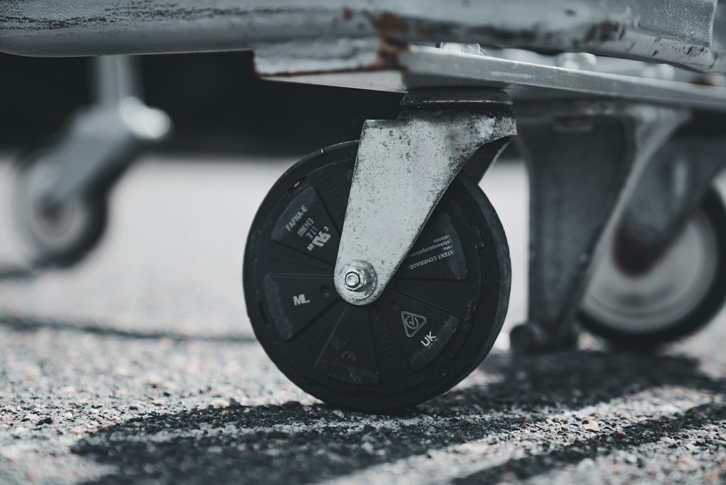 Worn black caster wheel resting on textured grey asphalt.